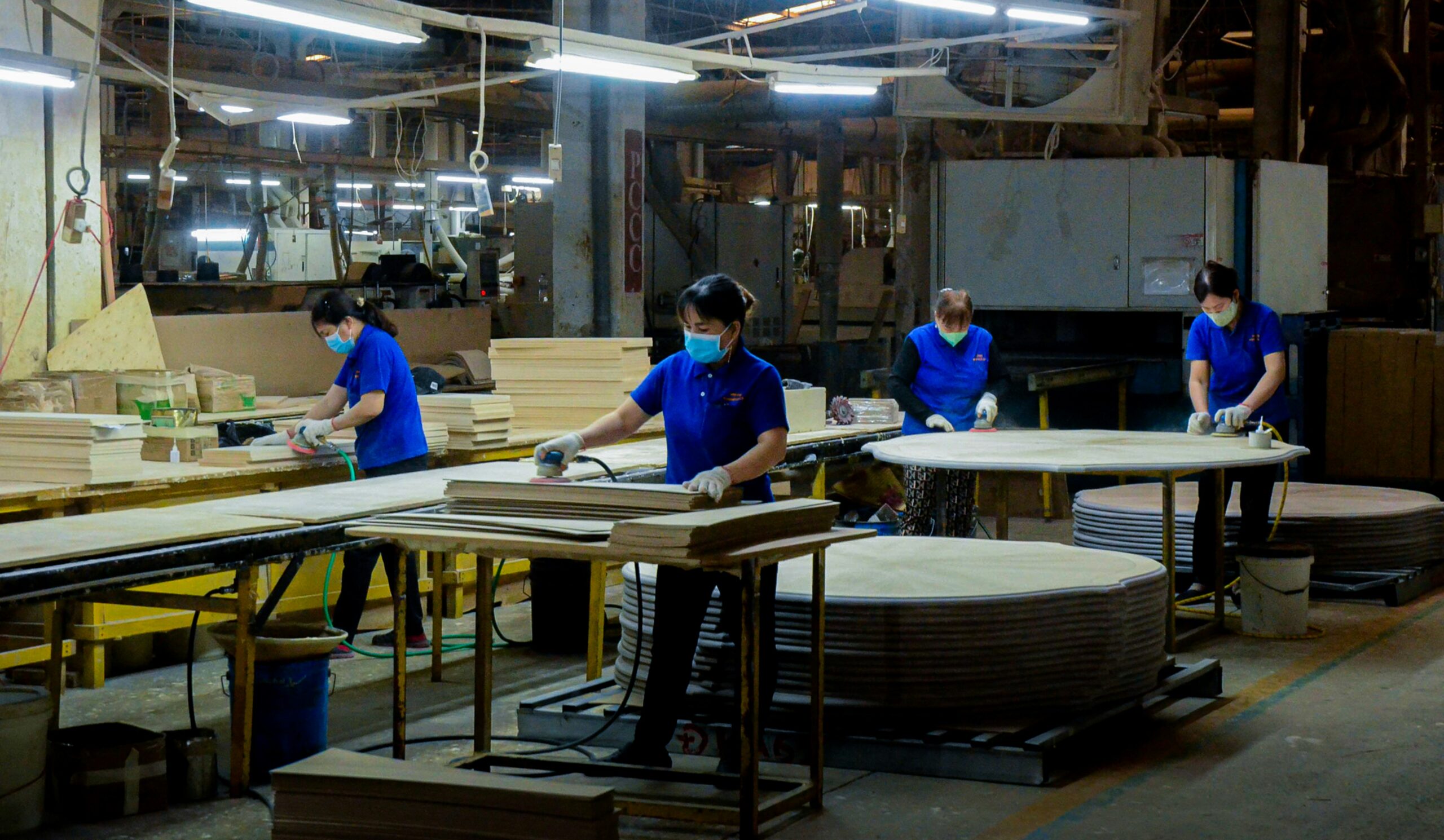 Vietnamese furniture factory operating wood sanders on table tops.